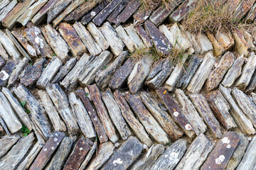 Rugged stone wall built from diagonal slabs creates rustic textured landscape feature in natural outdoor gardens