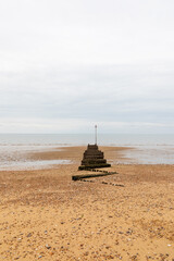 Fototapeta premium Minimalist beach breakwater waves stopper extending into calm sea under soft cloudy sky