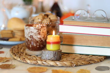 Lit candles, cookies, chocolate, nuts, tea, wine, pumpkins, books, reading glasses and autumn leaves on the table. Autumnal hygge at home. Selective focus.