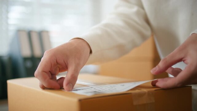 Close up of Business owner hand putting shipping label on parcel, preparing for delivery to customer. Small business shop owner Preparing online orders for shipping. inventory and order processing.