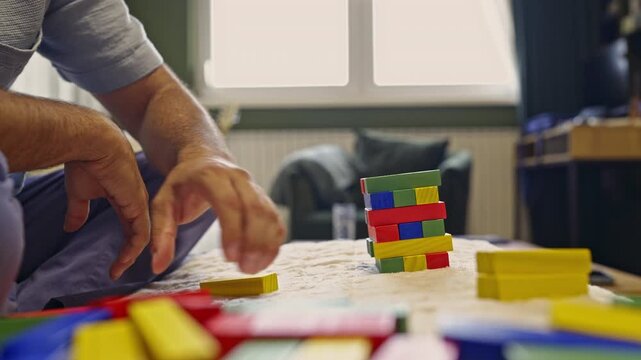 A man's hands carefully build a tower using colorful wooden blocks, showcasing concentration and precision. This relaxing video is accompanied by the satisfying sounds of play.