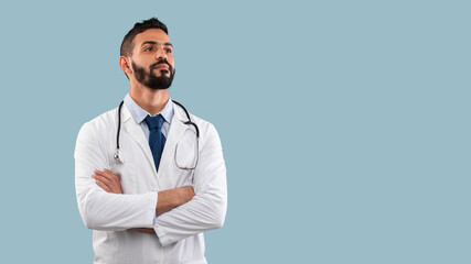 A doctor dressed in a white coat and tie stands confidently with arms crossed. He appears prepared to assist patients, offering a professional demeanor against a light blue background.