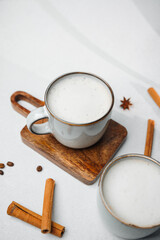Warm creamy drinks with cinnamon sticks and anise on a light surface