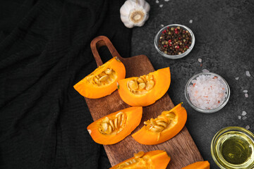 Orange pumpkin slices with spices and olive oil on a dark background, preparing for cooking.