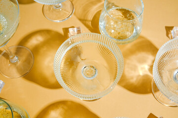 Sparkling drinks in clear glasses with ice cubes on a yellow background, creating dramatic shadows.