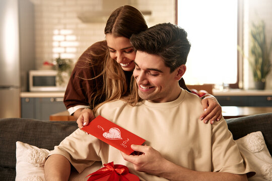 Happy couple celebrating Valentine's Day at home with card and heart-shaped gift box
