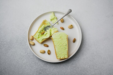 Pistachio ice cream cones on a plate with scattered nuts and a spoon.