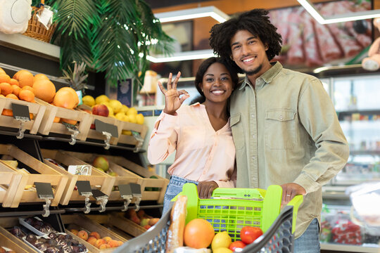 Couple enjoys a fun shopping experience in a colorful grocery store filled with fresh fruits and vegetables. They display excitement as they select healthy items. - Powered by Adobe
