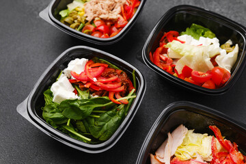 Mixed salads with fresh vegetables meat cheese and greens in black containers for restaurant delivery or meal prep concept