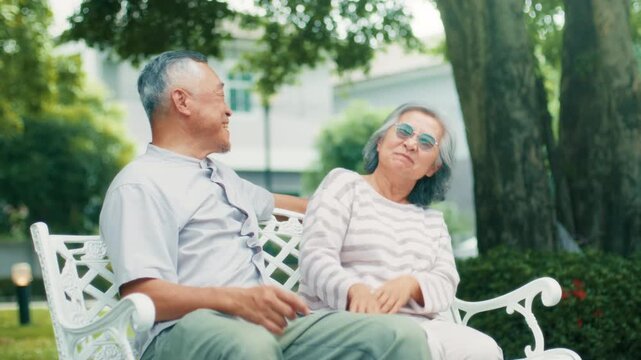 retired Asian couple woman and man hugging together on bench in park. Happy senior couple husband and wife resting, talking and bonding together, sharing romantic moment outdoors. retirement concept.