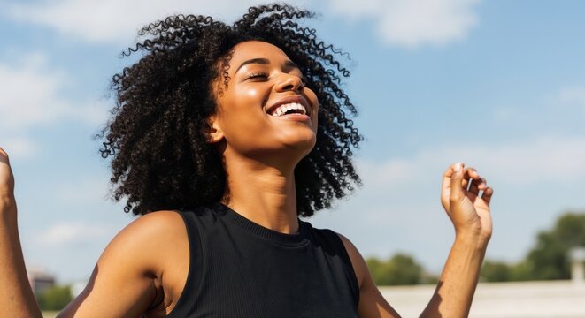 Happy young black woman smiling in the sun. Portrait of a joyful african american person with natural curly hair outdoors. Well-being and freedom concept