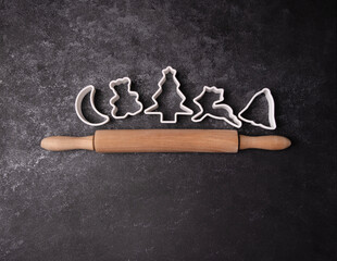 Christmas cookie cutters and a rolling pin on a dark textured background, space for text
