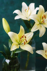 Obraz premium Elegant white lilies in glass vase on green background – floral decor or wellness concept