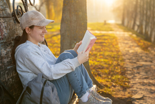 A happy 31 year old caucasian brunette woman reads a book while sitting on a park bench