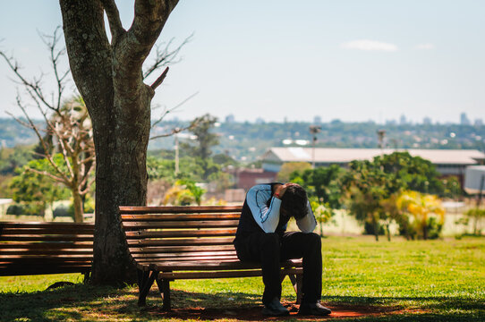 Hombre joven sentado solo en el banco de la plaza, pensando y reflexionando sobre su vida, ansiedad