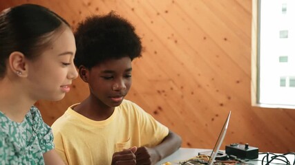 Site view of african boy and caucasian girl in casual cloth working together to coding prompt or programming system at table with laptop and electronic equipment at STEM technology class. Edification