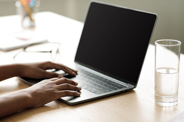 A teenage afro American girl sits at a desk typing on a laptop with an empty screen. She is focused on her studies, learning from home in a quiet and modern interior.
