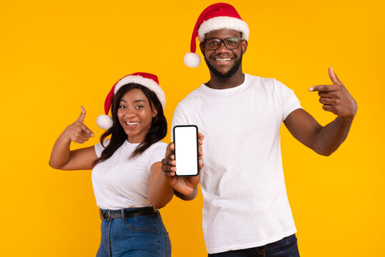 A joyful black couple wears Santa hats and gestures thumbs up while showing an empty smartphone screen. - Powered by Adobe