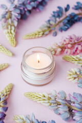 Burning candle surrounded by lupin flowers on pink background