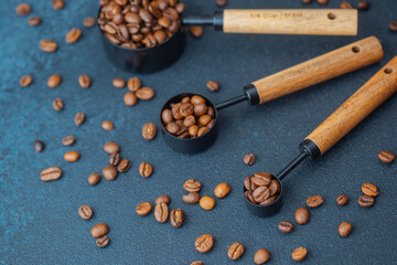 Coffee beans in measuring spoons on dark background