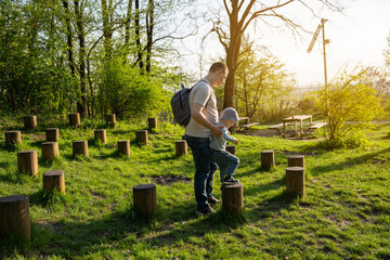 A young father and her four year old toddler son walk on logs and have fun while having fun in a park or forest on a sunny spring day. Family spending time and lifestyle