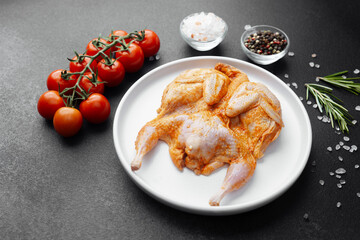 Marinated quail on white plate with fresh tomatoes, salt and spices on black background