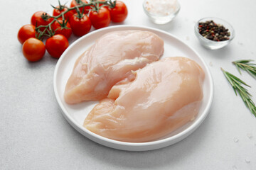 Raw chicken breast on white plate with salt, pepper, rosemary and cherry tomatoes
