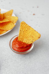 Crispy nacho chip in salsa bowl with plate of chips and fresh tomatoes