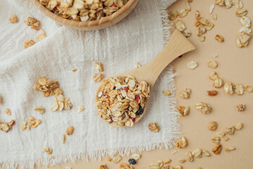 Granola scattered on white textile and spoon on beige background