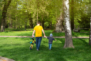 Fototapeta premium Father and son walking in the park holding hands on a sunny spring day. Family time and leisure. Lifestyle