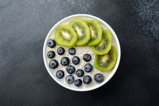 Oatmeal bowl with kiwi and blueberries with assorted fruit on black table - Powered by Adobe