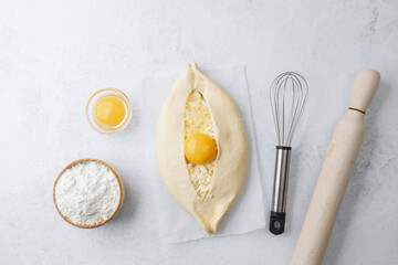 Uncooked khachapuri with egg yolk and whisk on white background