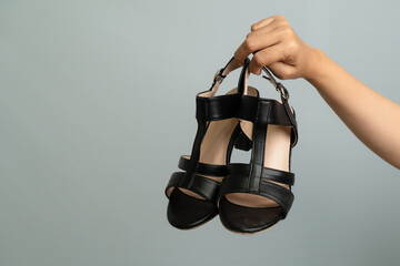 Close up Of A Hand Holding Black High Heel Shoes Against A Light Blue Background