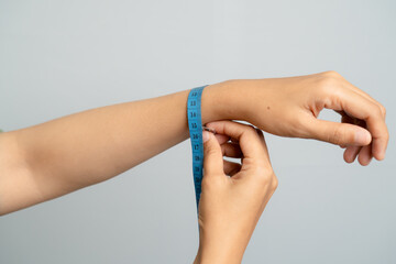 Close Up of a Woman Measuring Her Wrist Circumference with a Blue Tape Measure against a Soft Gray Background