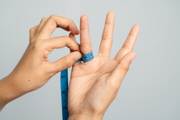Close Up Of Hands Measuring Finger Size With Blue Measuring Tape On Gray Background