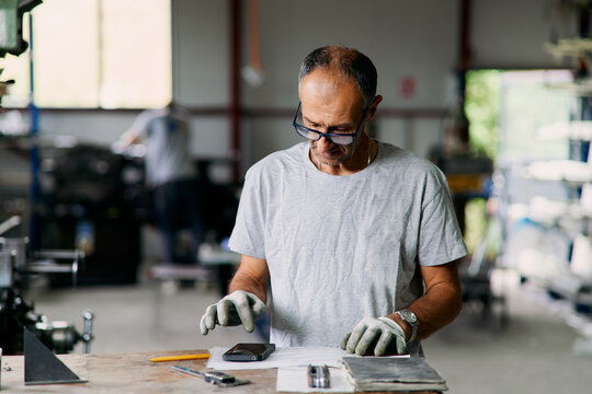 Craftsman Inspecting Smartphone On Workbench In Workshop With Tools Pe