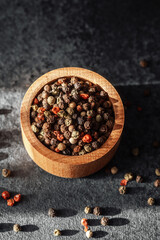 Colorful assortment of whole peppercorns in wooden bowl on dark surface