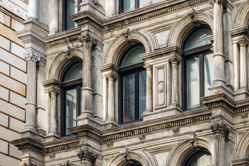 A detailed view of a historic stone facade in downtown Montreal, featuring arched windows, classical columns, ornate carvings, and rich architectural textures.
