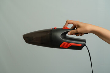 Hand Holding A Black Handheld Vacuum Cleaner With Red Accents Against A Light Gray Background
