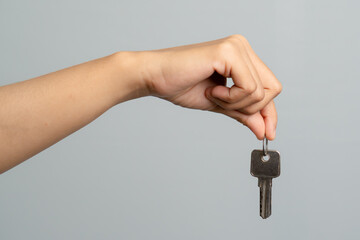 Hand Holding a Single Silver Key Isolated On A Plain Gray Background
