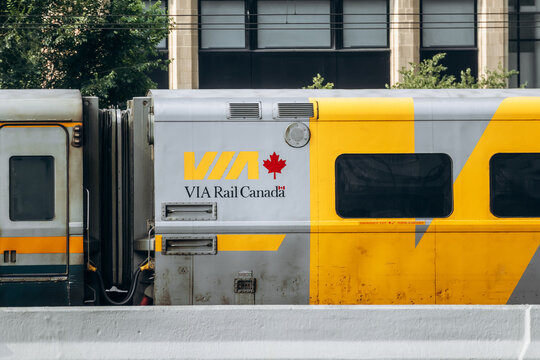 Montreal, Canada - August 14, 2025: A close view of a VIA Rail Canada train in downtown Montreal, showing the yellow and grey livery with the maple leaf logo and the connection between two cars.