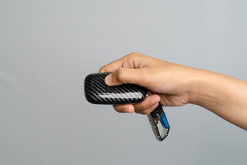 Hand Holding Black Carbon Fiber Car Key Fob With Carabiner Clip On Plain Background