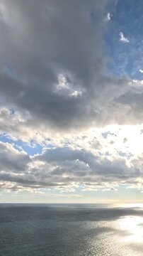 Ocean, Sky, Clouds vast expanse under dynamic partly cloudy blue sky, sunlight reflecting on shimmering water surface. Vertical video.