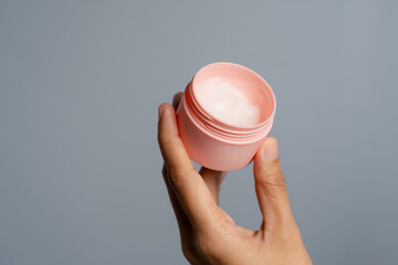Hand Holding Open Pink Jar Of Cream On Gray Background Studio Shot