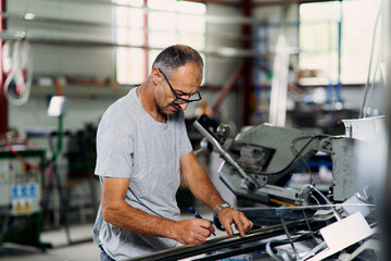 Fototapeta premium Factory worker examining metal material in industrial workshop, representing quality control, inspection, and manufacturing process.