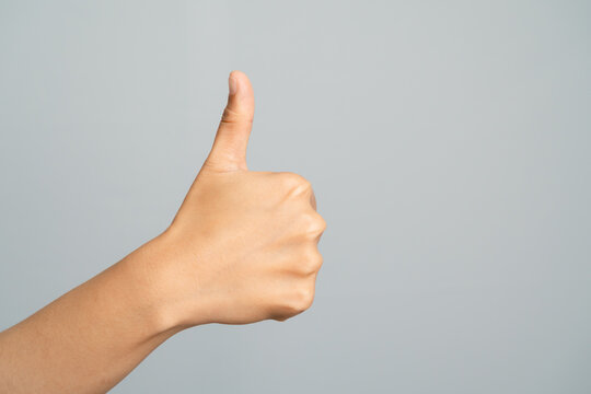 Hand Showing Thumbs Up Gesture With Light Skin Tone Against A Light Gray Studio Background