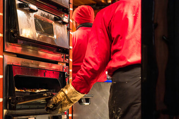 Street market scene showing baker pulling a tray of food from an industrial oven at a food market or bakery stand.
