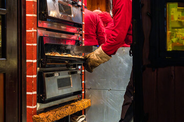 Street market scene showing baker pulling a tray of food from an industrial oven at a food market or bakery stand.
