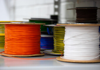 a close-up view of various spools of electrical wire in bright colors, including green, red, yellow, and orange. The reels are arranged on a workbench in a workshop environment, creating a technical a