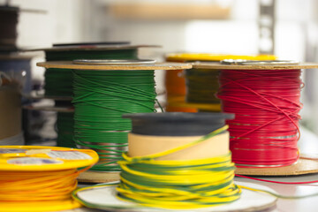 a close-up view of various spools of electrical wire in bright colors, including green, red, yellow, and orange. The reels are arranged on a workbench in a workshop environment, creating a technical a